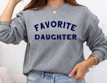 Load image into Gallery viewer, A person wearing a heather gray crewneck sweatshirt with the words 'FAVORITE DAUGHTER' printed in navy blue across the chest, paired with light blue jeans.